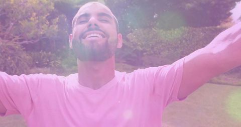 Smiling Man in Sunlit Park in Pink Shirt Embracing Nature