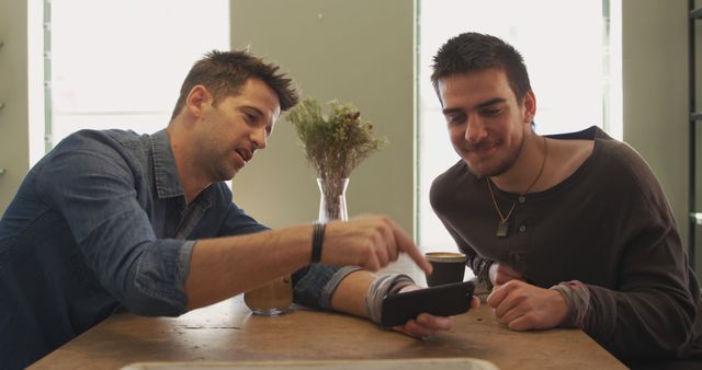 Two Young Men Enjoying Coffee While Looking at Smartphone Screen at Café Table - Download Free Stock Images Pikwizard.com