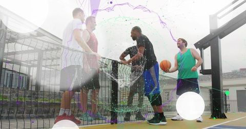 Rooftop basketball crew talking while holding ball by chain-link fence on urban court