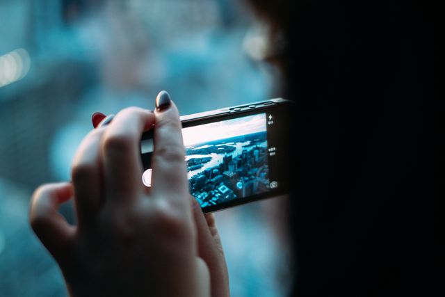 Person holding a smartphone, capturing an urban cityscape from a high-rise building angle. Perfect for use in travel blogs, tourism industry promotions, smartphone advertisements, and city lifestyle articles.