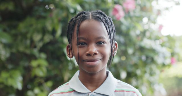 Smiling boy with braided hair standing with nature in the background. Perfect for themes related to childhood, happiness, outdoor activities, innocence, casual lifestyles, and nature's beauty. Can be used in educational materials, family and parenting topics, advertisements, and websites focused on youth and well-being.