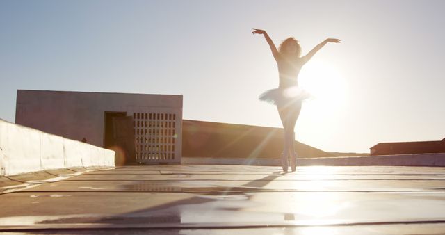 Side view of a biracial female ballet dancer practicing on rooftop at sunrise, walking on tiptoes and turning around.