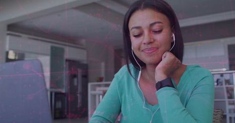 Smiling woman working remotely at modern kitchen desk with laptop, earbuds and smartwatch