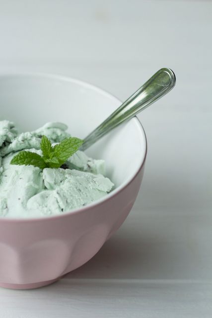 Mint green ice cream served in pink bowl with silver spoon. Fresh mint topping enhances visual appeal. Ideal for food blogs, summer menus, dessert advertising, and culinary presentations.