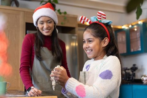 Mother daughter kneading holiday dough in kitchen wearing santa hat and festive headband