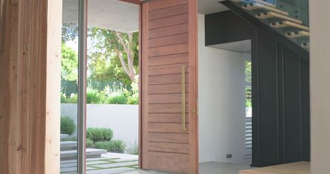 Welcoming modern entryway with oversized wooden pivot door opening onto sunlit courtyard