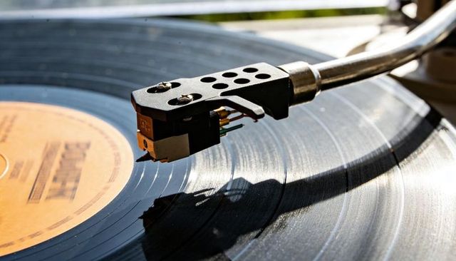 Sunlit turntable tonearm tracking vinyl record grooves on balcony closeup retro vibes