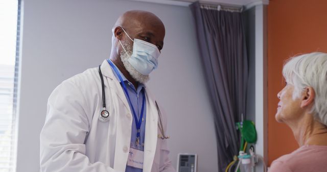 An experienced doctor wearing a white coat and a face mask examines an elderly patient in a hospital room. Ideal for use in healthcare and medical websites, articles related to elderly care, healthcare services, and hospital environments. Suitable for brochures and educational materials that promote health services for seniors.