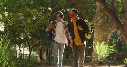 Couple Walking Hand in Hand with Backpacks in Sunny Park
