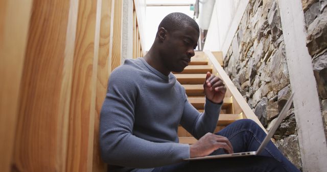 Focused Man Working on Laptop in Stairwell with Stone Wall - Download Free Stock Images Pikwizard.com