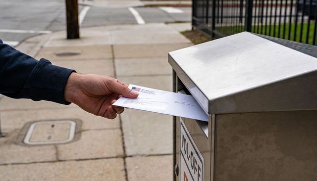 Hand inserting envelope into curbside mailbox for urban mailing, close-up postal drop