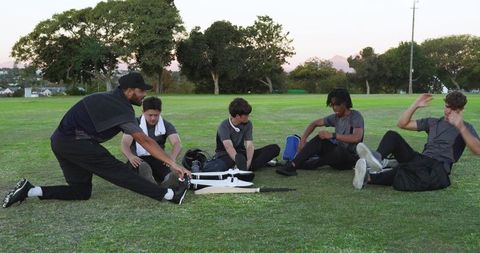 Coach leading diverse youth team performing warmup stretches on grassy field with bat