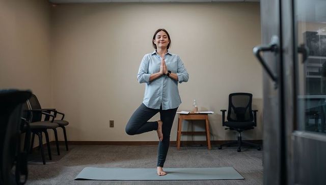 Practicing office yoga, woman balancing in tree pose on mat during mindful work break