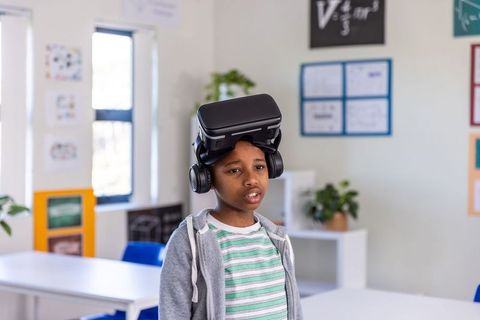 African american boy using vr headset and headphones in classroom for virtual learning