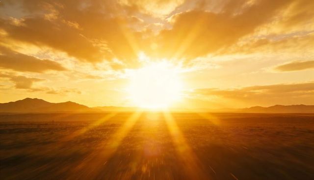 Sun sinking over arid plain with golden rays, lens flare, clouds and distant mountains