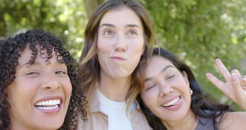 Diverse friends laughing and making silly faces while posing close in sunlit park