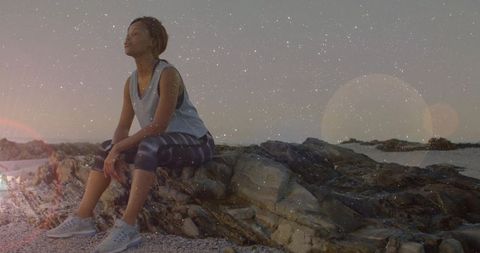Athletic woman resting on rocks by sea under starry sky