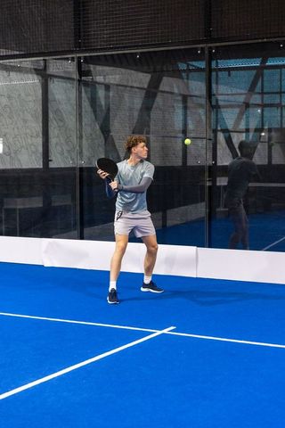 Light-skinned male athlete holding racket and preparing return shot on indoor padel court