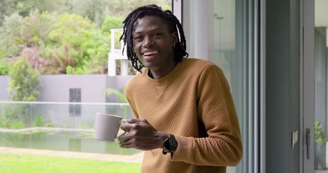 Smiling African American Man Holding Coffee Mug by Sliding Door Wearing Tan Sweater