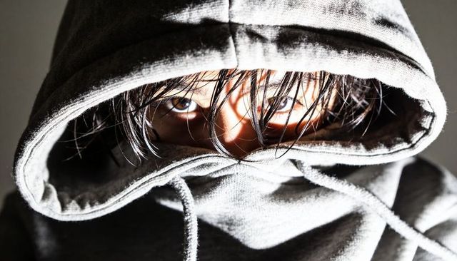 Staring hooded figure with intense gaze, wet hair and covered mouth dramatic portrait
