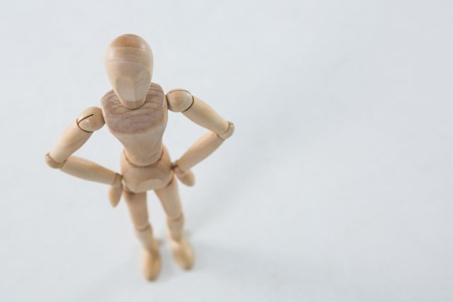 Wooden figurine standing with hands on hip on wooden background