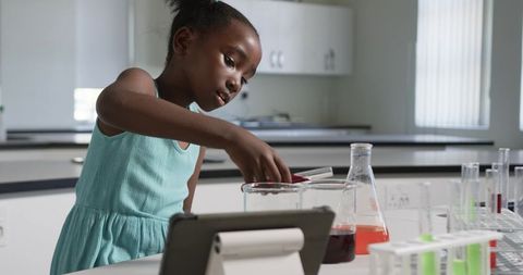 Young girl conducting hands-on chemistry experiment in school lab with tablet and colorful liquids