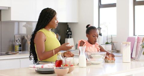 African american mother and daughter baking together in bright minimalist kitchen