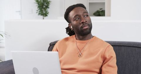African American man working remotely on laptop in minimalist living room, modern home office