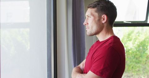 Thoughtful Man in Red Shirt Looking Out Window at Home
