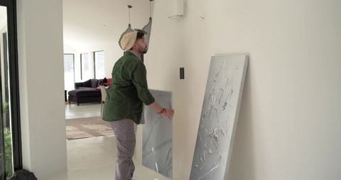 Indian man placing large abstract canvas on white wall in modern minimalist hallway