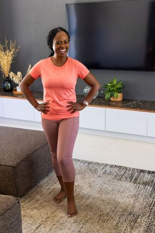 Smiling african woman wearing coral tee and mauve leggings in modern minimalist living room