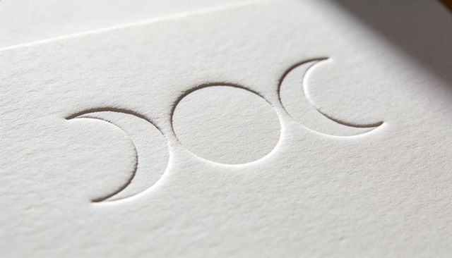 Showcasing Embossed Triple Moon Motif on Thick Off-White Cardstock with Soft Lighting