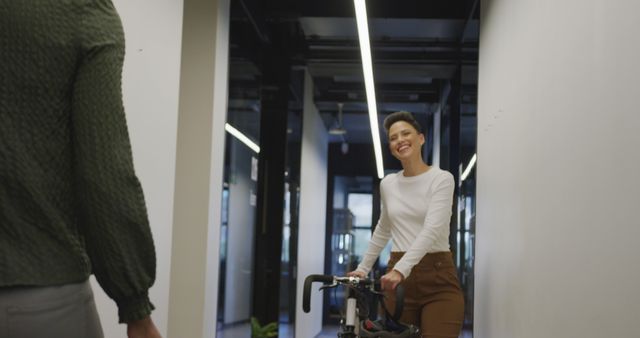 Woman walking with bicycle in modern office hallway showing combination of sustainable transportation and professional environment. Ideal for illustrating articles on workplace wellness, sustainable commuting, or casual workspaces.