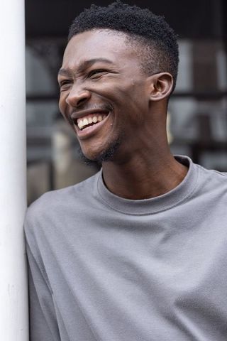 African adult male laughing and leaning on pole urban outdoor lifestyle portrait