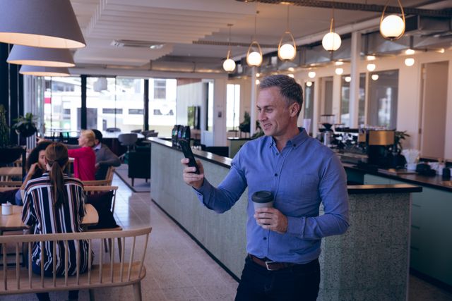 Caucasian professional businessman working in a modern creative office, taking a break using smartphone in an office canteen. Business creativity technology.