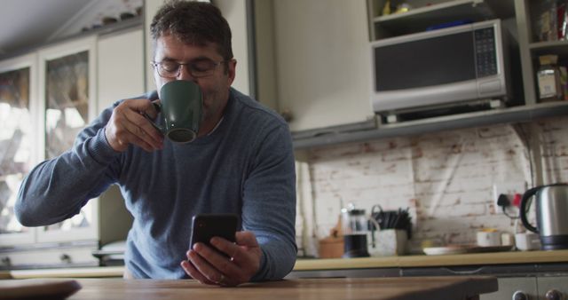 Man drinking coffee using smartphone in kitchen - Download Free Stock Images Pikwizard.com