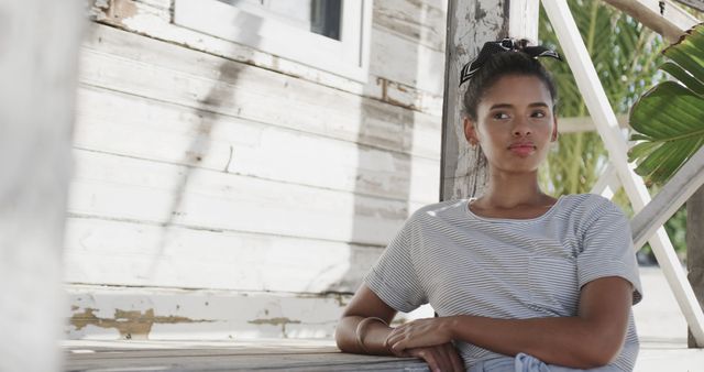 Biracial woman leaning on table outside house on beach, copy space. Lifestyle, nature, relaxation, vacation, summer and leisure, unaltered.