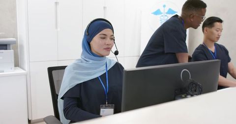 Multicultural medical reception team assisting patients via headset at clinic front desk