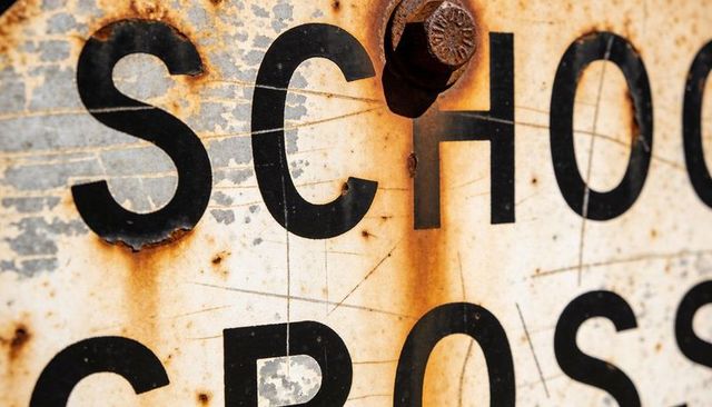 Close-up rusted school crossing sign showing corroded hex bolt, weathered letters and texture