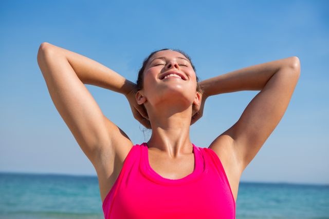 Smiling young woman with eyes closed exercising at beach on sunny day