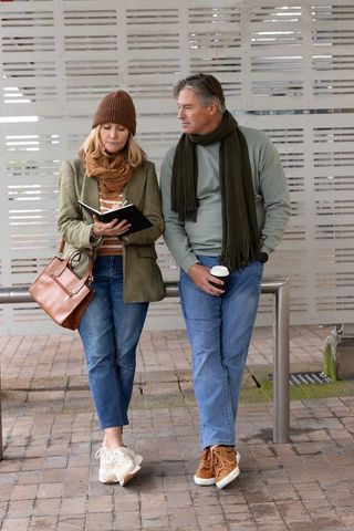 Middle-aged couple standing at transit stop writing in journal holding coffee urban lifestyle