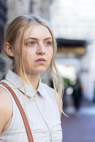 Thoughtful woman on urban sidewalk wearing sleeveless collared top and brown crossbody bag