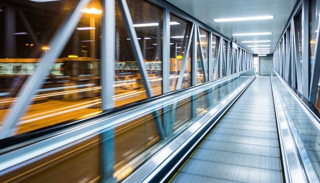 Empty moving walkway in glass airport jetbridge at night, futuristic transit perspective