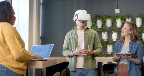 Team testing vr headset while collaborating with laptop and tablet in green workspace