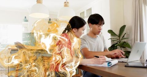 Young couple working from home typing on laptop and writing notes with gold abstract overlay