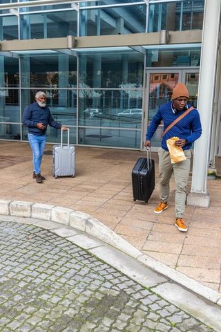 African american men walking pulling luggage outside modern glass office building
