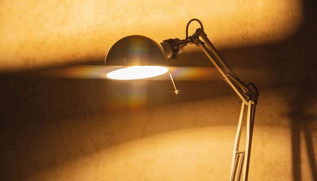 Emitting adjustable desk lamp with dome shade casting warm amber glow and wall shadows
