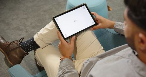 Indian man relaxing in coworking lounge holding tablet with blank screen for app mockup