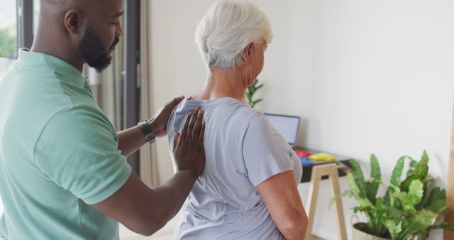 This image can be used in health and wellness websites, blogs on senior care, physiotherapy promotional materials, and healthcare service brochures. It illustrates the importance of physical therapy for the elderly, showing a physiotherapist helping a senior woman with back exercises in a home environment.