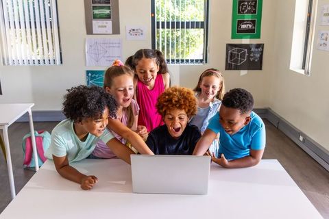 Diverse children gathering around laptop, discovering and collaborating in classroom